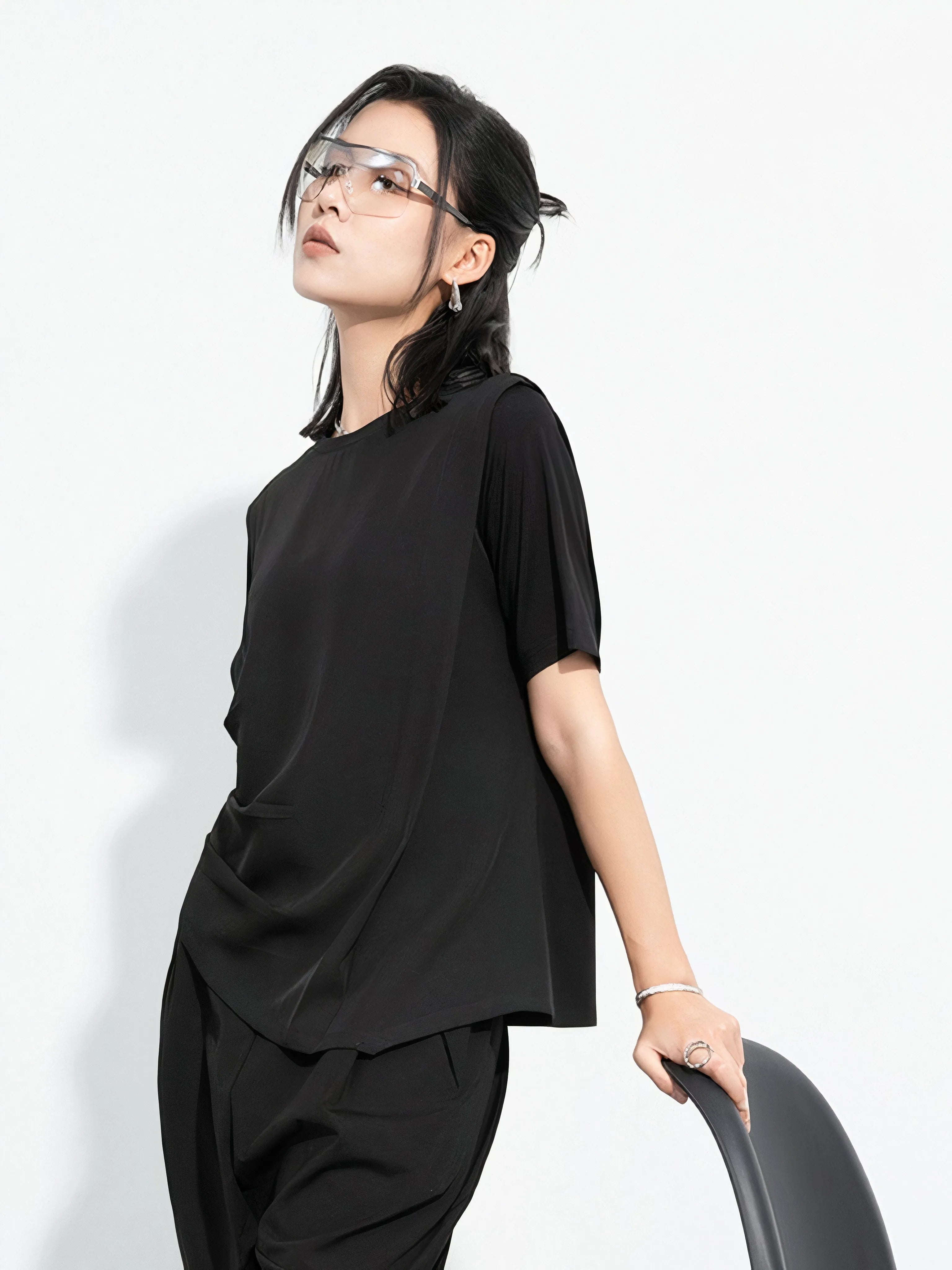 Black minimalist Japandi-style top worn by a woman, asymmetrical design and oversized fit, product by Sumoka Studio.